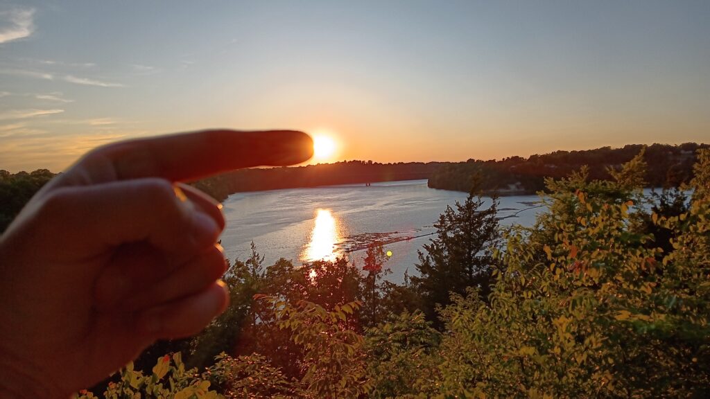 Sun appears like a light at the end of a finger like the iconic ET movie poster with a forest and lake in the background