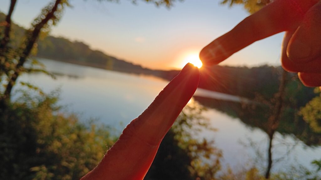 Sistine chapel like picture in nature with sun between two fingers about to touch with a forest and lake in the background